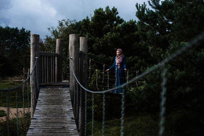 Woman standing on footbridge against trees