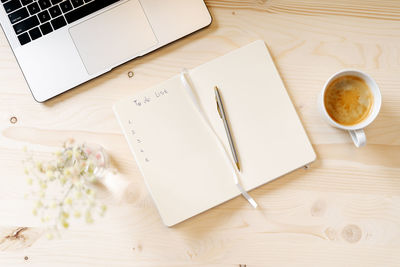Top view blank paper notebook with to do list, laptop keyboard, cup of coffee and pen. desktop mocku