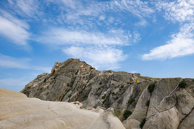 Man resting on rock formations against sky