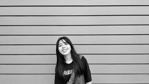 Portrait of smiling young woman standing against wall