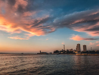 Sea by buildings against sky during sunset