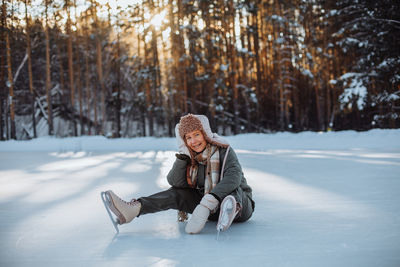 Smiling young blonde girl in a hat with earflaps and a green suit posing on a skating rink