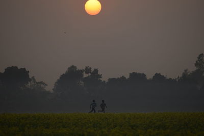 Silhouette men on field against clear sky during sunset