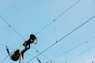 Low angle view of public address system by cables against clear blue sky