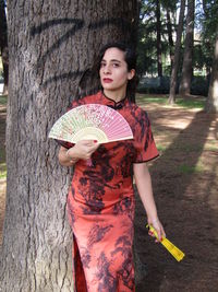 Portrait of young woman standing on tree trunk