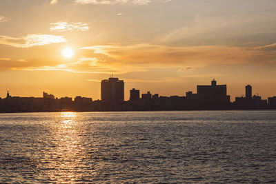 Sea by buildings against sky during sunset