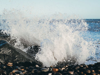 Waves splashing on rocks at shore against sky