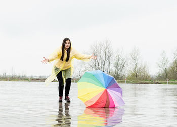 Beautiful brunette woman with funny face in yellow raincoat catching colorful umbrella