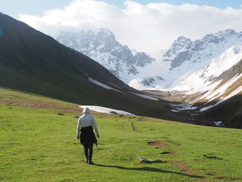 Rear view of man walking on field against mountains