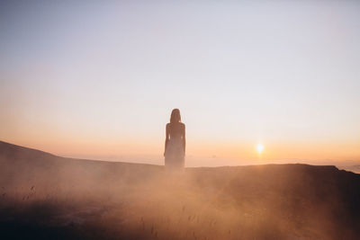 Rear view of young woman standing at field against clear sky