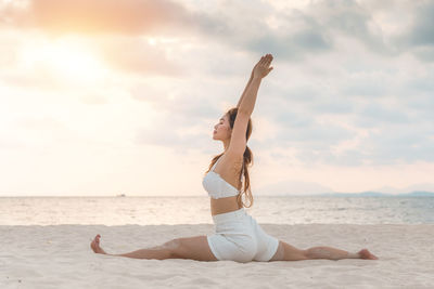 Full length of woman exercising on beach against sky