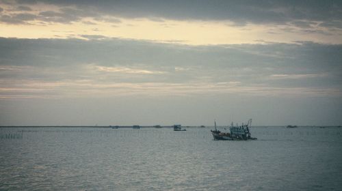 Fishing boat sailing in sea against sky during sunset