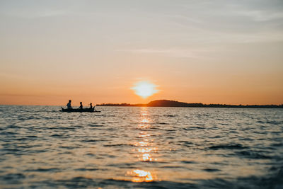 Silhouette people in sea against sky during sunset