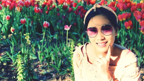 Portrait of smiling young woman against red tulips blooming on field