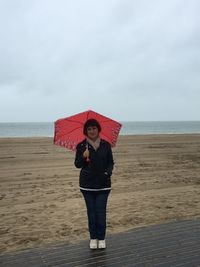 Portrait of mature woman with umbrella standing at beach against sky