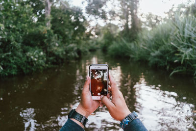 Man holding camera while standing by lake