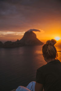 Woman sitting against sea during sunset