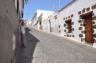 Woman walking on footpath amidst buildings against sky