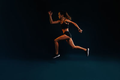 Full length of woman exercising against black background