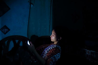 Side view of young woman sitting at home looking at her phone