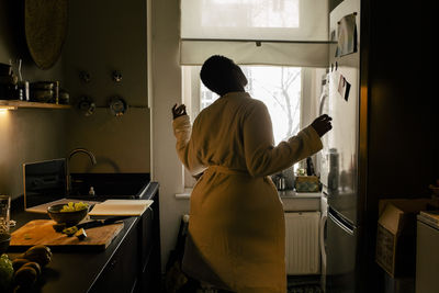 Carefree young woman wearing bathrobe dancing in kitchen at home