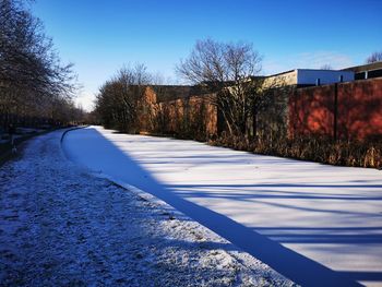 Snow covered road by trees against blue sky