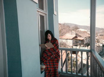 Woman reading book while sitting in balcony