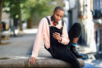 Young man using phone while sitting on railing