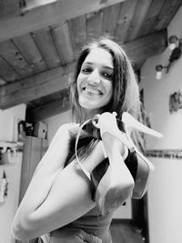 Portrait of smiling young woman holding high heels at home