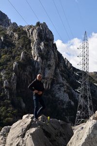 Man standing on rock by mountain against sky