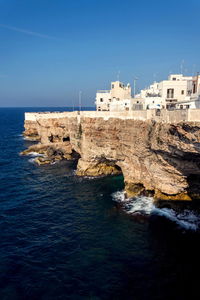 Buildings by sea against clear blue sky