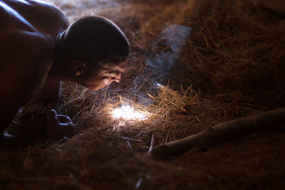 Shirtless man preparing fire on hay