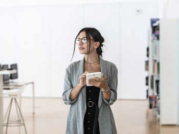 Female in glasses using tablet while standing in spacious workplace and working on project