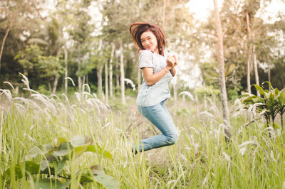 Portrait of smiling woman jumping by plants on field 