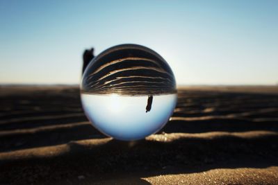 Close-up of crystal ball on beach against clear sky