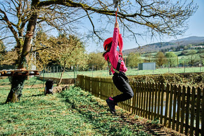 Little girl with protections practicing climbing between trees with ropes and nets