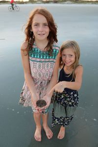 Portrait of smiling sisters showing sand dollar while standing on shore