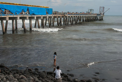 Rear view of people on pier at beach against sky