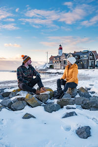 Couple sitting on rock against sky during winter