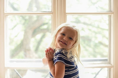 Portrait of smiling girl against window at home