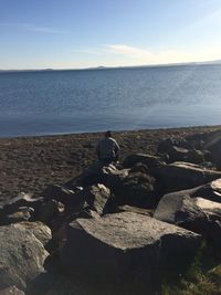 Man sitting on rock by sea against sky