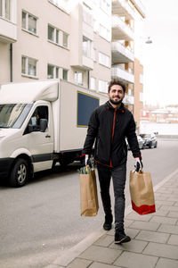 Confident young delivery man carrying grocery bags on street in city