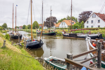 Sailboats moored on river by buildings against sky