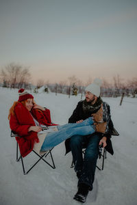 Full length of couple sitting on snow covered land during winter