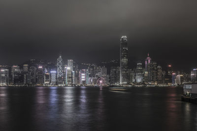 Illuminated buildings by river against sky at night