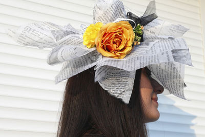 Close-up of smiling young woman wearing paper hat with artificial flowers against white wall