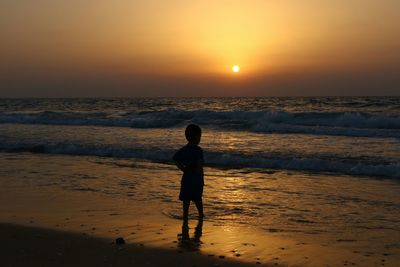Silhouette boy standing on beach against sky during sunset