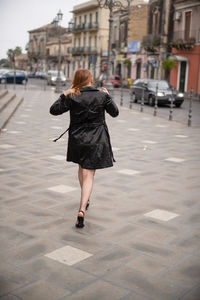 Rear view of woman walking on footpath in city