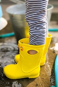 Kid's feet in yellow rubber rain boots in water on a rainy day