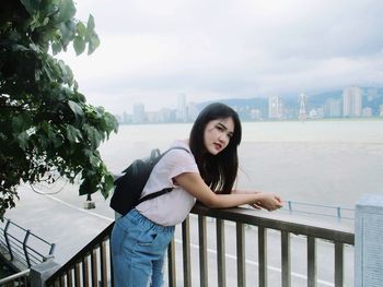 Portrait of smiling young woman standing against railing in city